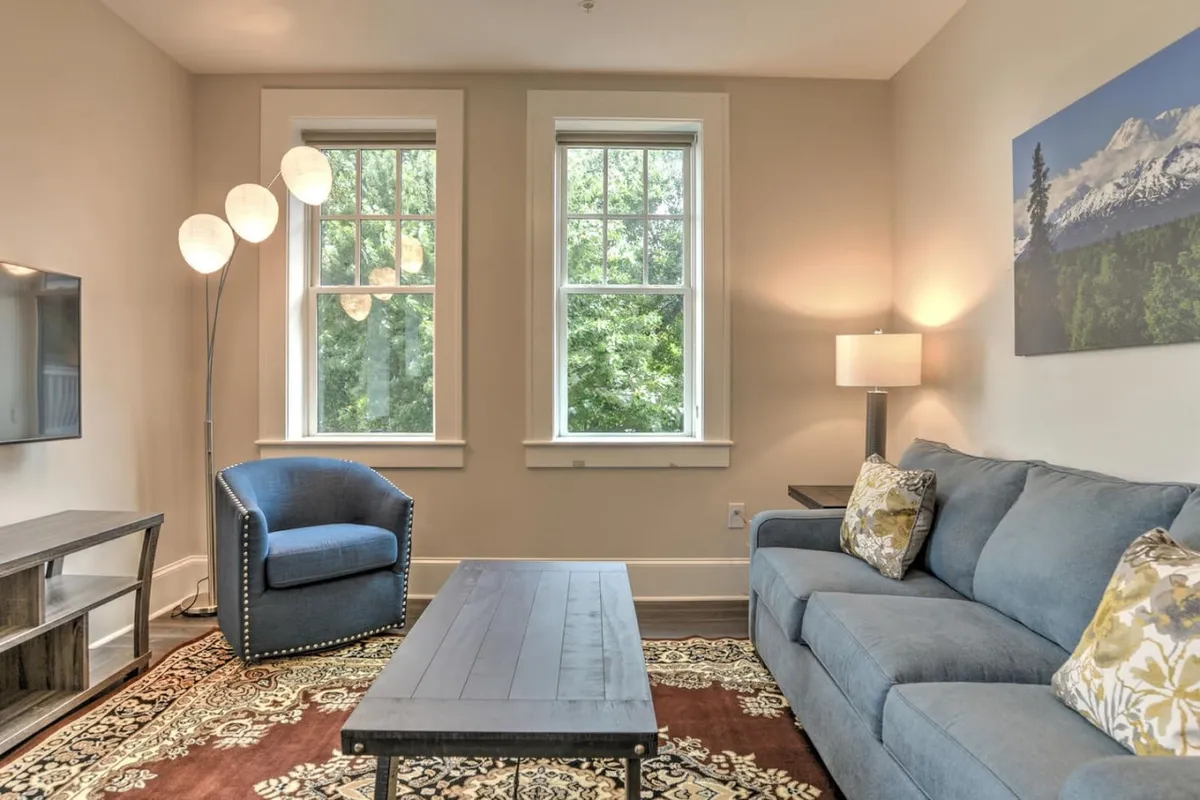 A warm, inviting living area featuring a comfortable sofa, armchair, and coffee table. The space is filled with daylight streaming through large windows, and highlighted by tasteful artwork and a stylish lighting fixture. The mood is cozy yet sophisticated, perfect for relaxing or socializing after a day exploring the city.