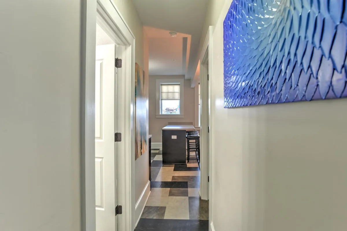 A welcoming kitchen area featuring blue wall art, a kitchen island, and eye-catching floor tiles. The layout is designed for shared meals and casual conversations, with artistic touches adding personality to the compact culinary space.