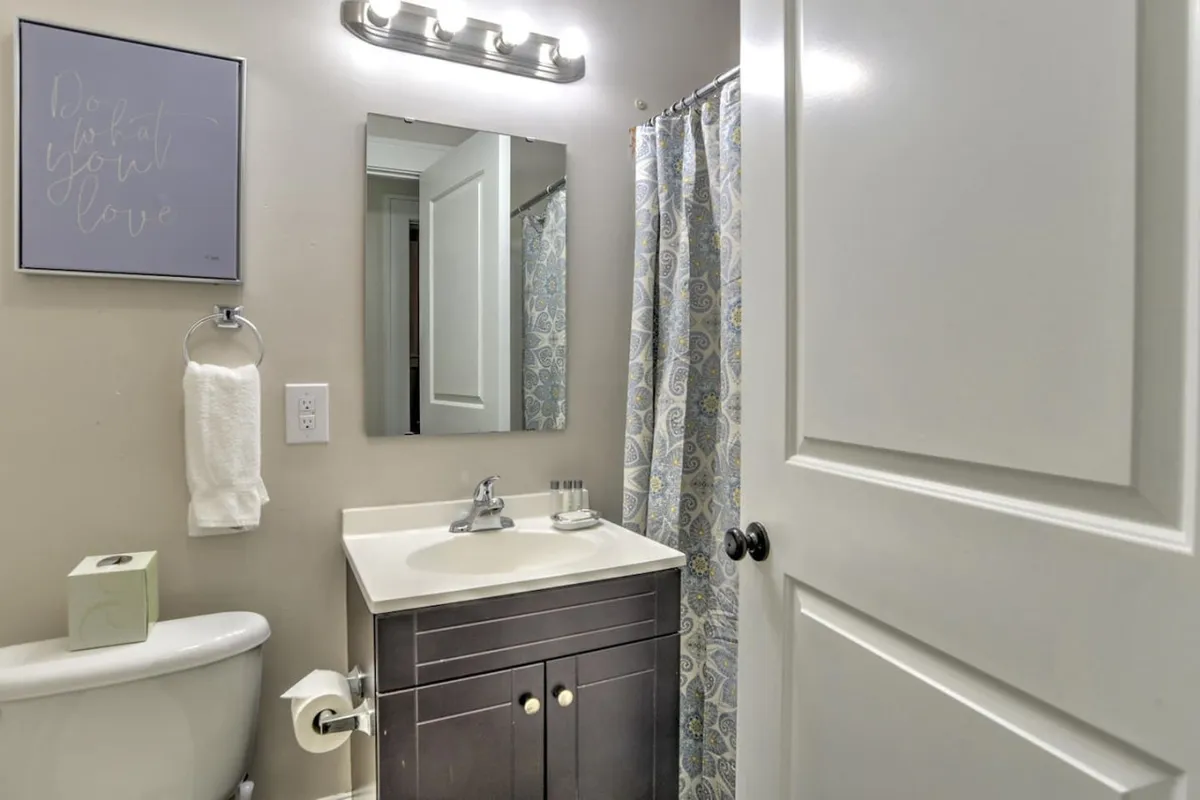 A calm and inviting bathroom featuring a stylish vanity with sink, a large mirror, a shower with a curtain, and tasteful framed wall art. The soft lighting and tidy arrangement evoke a sense of privacy and relaxation, ideal for both morning preparations and evening unwinding.