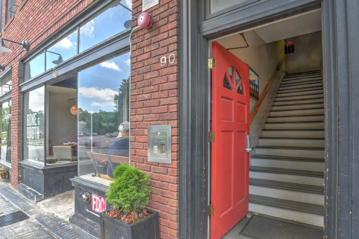The image captures the exterior of a charming historic building featuring a classic brick facade, a welcoming red door, and large windows that hint at the inviting atmosphere within. People can be seen visiting a nearby eatery, socializing with friends, and exploring the neighborhood, adding a sense of vibrancy and local connection.